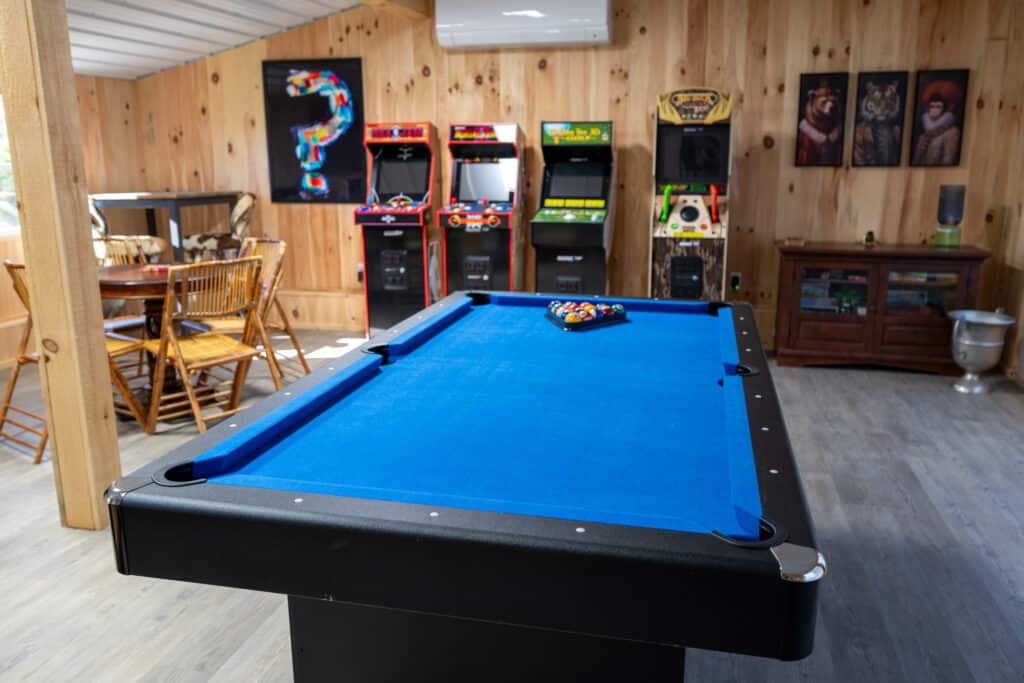 Rustic game room with blue pool table, retro arcade machines, and warm wooden decor.