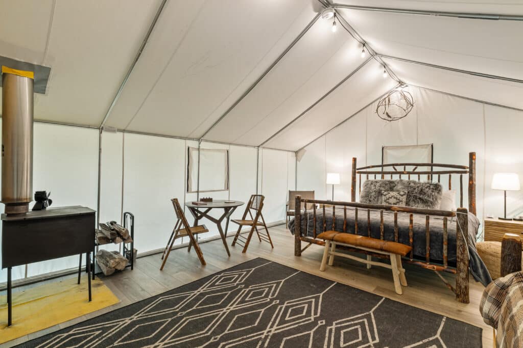 Luxury glamping tent interior with rustic wooden bed, warm lighting, and cozy outdoor retreat decor.