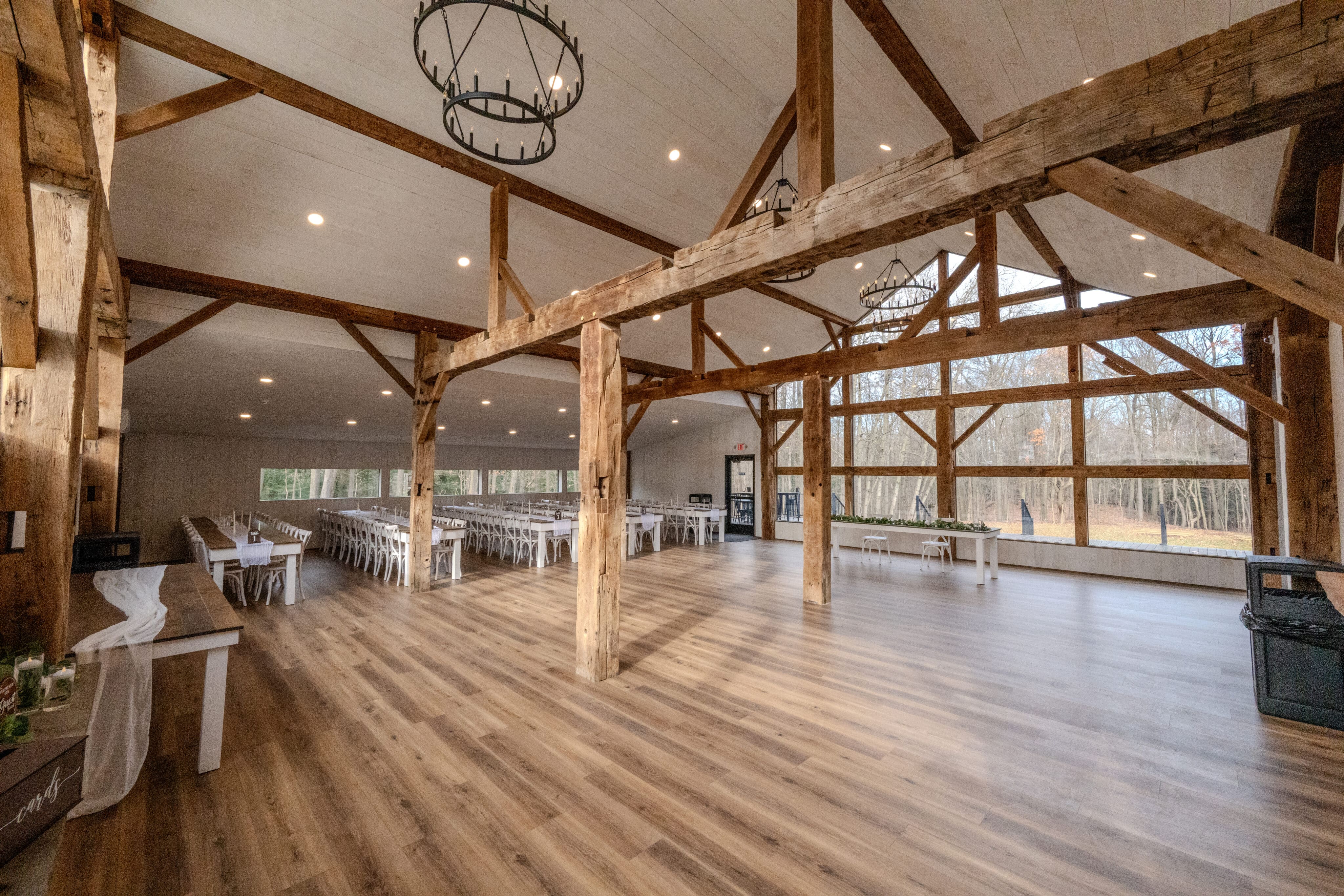 Rustic barn event hall with wooden beams, chandeliers, and white chairs ready for a ceremony.