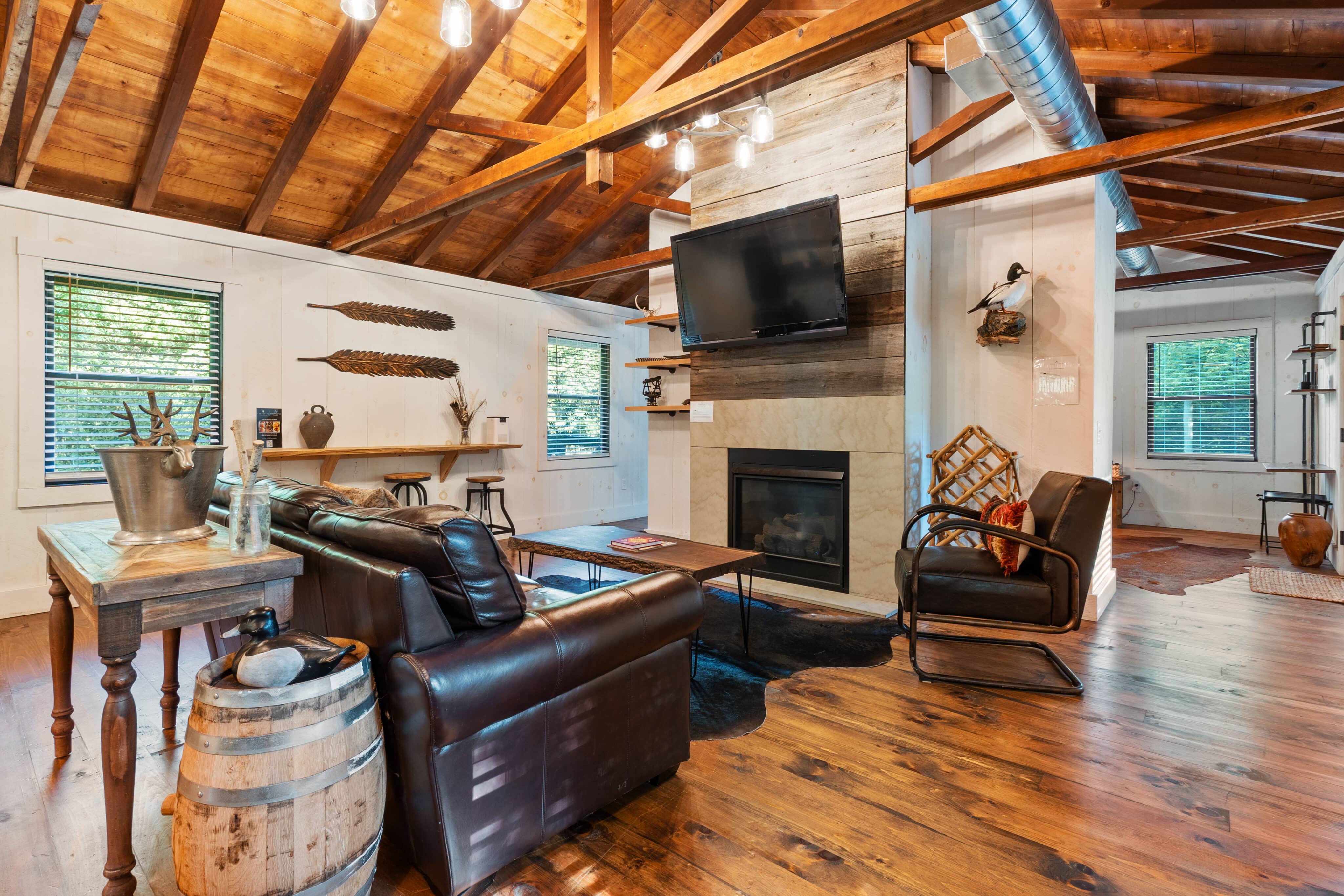 Rustic cabin living room with leather furniture, wooden beams, and a stone fireplace.